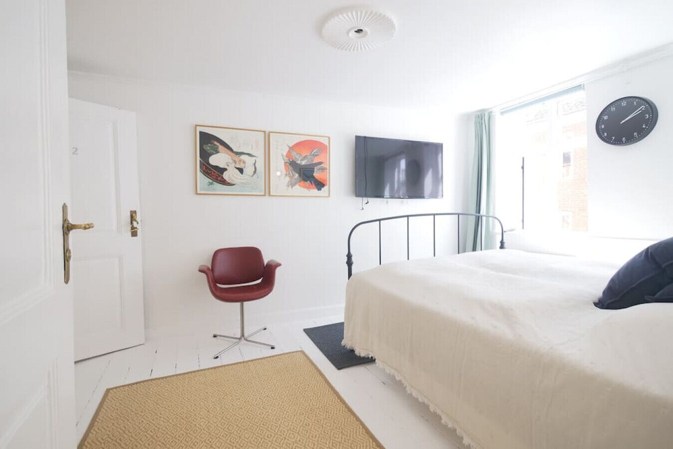 Un dormitorio con cama, una silla, televisión y obras de arte en la pared.