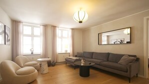 A modern living room with a grey sofa, beige armchairs, a round coffee table, and a white side table.