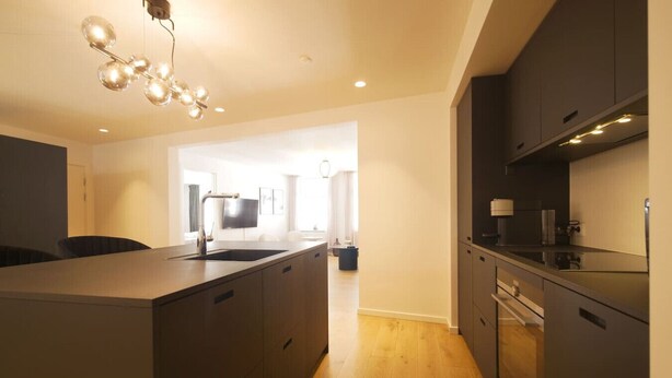 A modern kitchen with a central island, dark cabinetry, and a hanging light fixture.