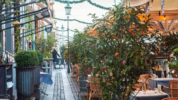 An outdoor café with tables and chairs, surrounded by greenery and buildings. - New Harbour / Carolina's Apartments / 2 BR (København)