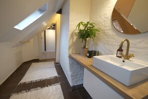 Ein modernes Badezimmer mit Oberlicht, einem weißen Waschbecken und einem Blumentopf.