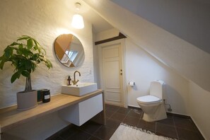 A modern bathroom with a white vanity, a round mirror, a potted plant, and a toilet.