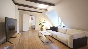 Een moderne woonkamer met een televisie, bank, salontafel en een plant.