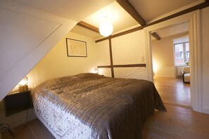 Ein Schlafzimmer mit schrägen Wänden, einem Bett mit strukturierter Decke, einer Nachttischlampe und einem gerahmten Bild an der Wand.