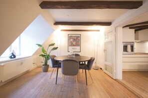 A dining area with a round table, chairs, a potted plant, and a painting on the wall.