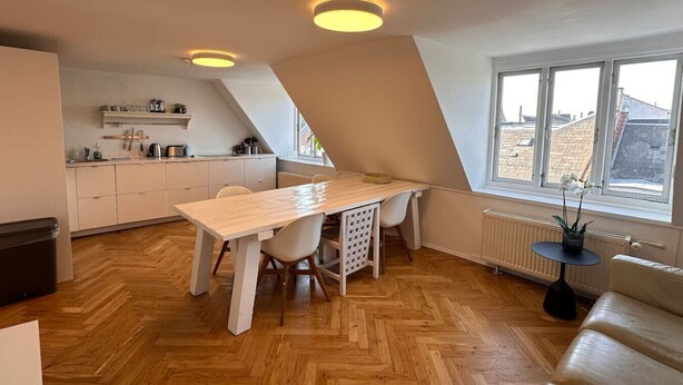 A modern kitchen with a wooden table and chairs, a built-in oven, and a window with a view of the city.