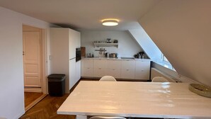 A compact kitchen with white cabinets, a dining table, and a trash bin.