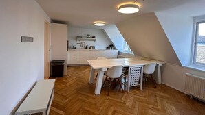 A modern kitchen with white cabinets, a wooden herringbone floor, and a dining area with a white table and chairs.
