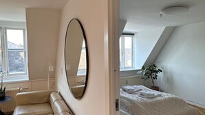 A bedroom with a large mirror, a bed with white bedding, a wooden bench, and a potted plant.