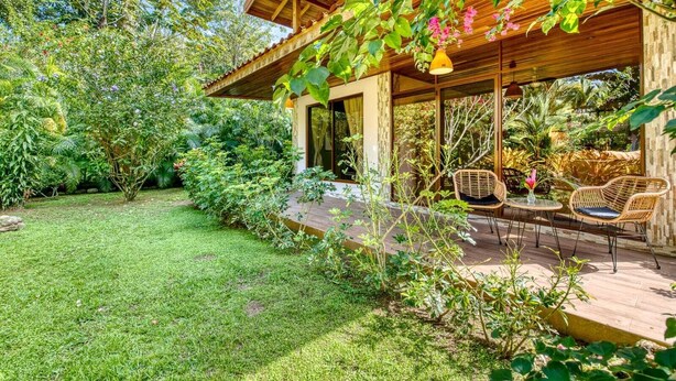 A covered outdoor seating area with a wooden deck, surrounded by lush greenery and a well-maintained lawn. - lazy parrots' luxury apartment#1: ✔pool ✔beach path✔AC (Puerto Viejo de Talamanca)