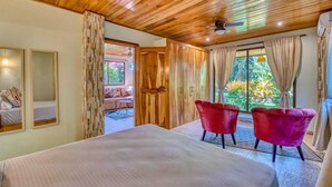 A bedroom with a large bed, wooden ceiling, two red chairs, and a view of the outdoors. - lazy parrots' luxury apartment#1: ✔pool ✔beach path✔AC (Puerto Viejo de Talamanca)