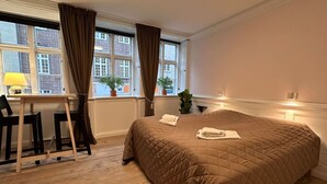 Ein Hotelzimmer mit einem großen Bett, einem Schreibtisch mit Stuhl, einem Fenster mit Vorhängen und einer Zimmerpflanze.