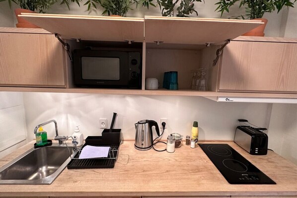 Une cuisine compacte équipée d’un évier, d’un four à micro-ondes, d’une bouilloire, d’un grille-pain et d’une plaque de cuisson intégrée.
