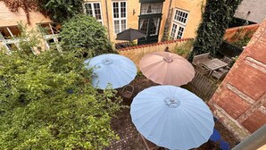 A courtyard with three umbrellas, a brick wall, and a wooden table.