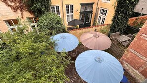 Een binnenplaats met drie parasols, een bakstenen muur en een gebouw met ramen en een deur.