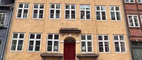 A multi-story building with a central red door, multiple windows, and a brick facade.