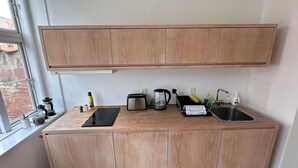 Cocina compacta con armarios de madera, estufa integrada, hervidor, tostadora y lavamanos.