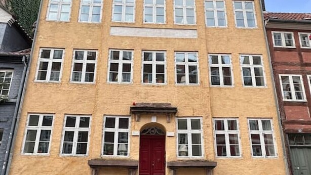 Un edificio de varios pisos con una puerta roja central, múltiples ventanas y fachada de ladrillo.