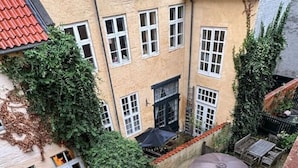 Une cour bordée de plusieurs parasols, un bâtiment avec des toits couverts de tuiles rouges et un mur de briques.