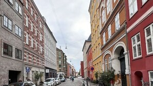 Une rue pavée bordée de bâtiments historiques, dont certains arborent des enseignes visibles et devant lesquels sont garées des voitures.