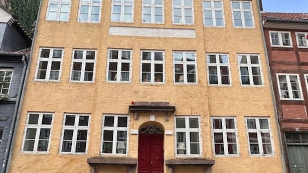 Un immeuble à plusieurs étages, doté d’une porte rouge au centre, de nombreuses fenêtres et d’une façade en briques.