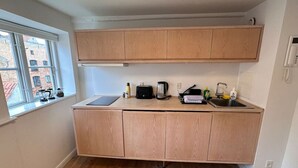Une cuisine de taille réduite, avec des meubles de rangement en bois, un plan de travail et une fenêtre donnant sur des immeubles.