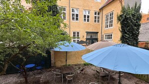 Eine Außenpatio mit Ziegelboden, Metallstühlen und -tischen unter blauen Sonnenschirmen.