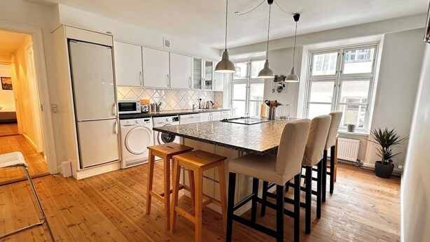 A modern kitchen with a granite countertop, wooden stools, and pendant lighting. - Main shopping street RAP 7 (København)