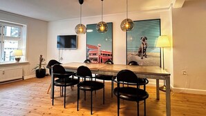 A dining area with a wooden table and black chairs, a TV mounted on the wall, and a painting of a dog on the wall. - Main shopping street RAP 7 (København)
