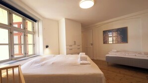 A bedroom with a large bed, a bedside table, a dresser, a window with blinds, and a painting on the wall. - Main shopping street RAP 7 (København)