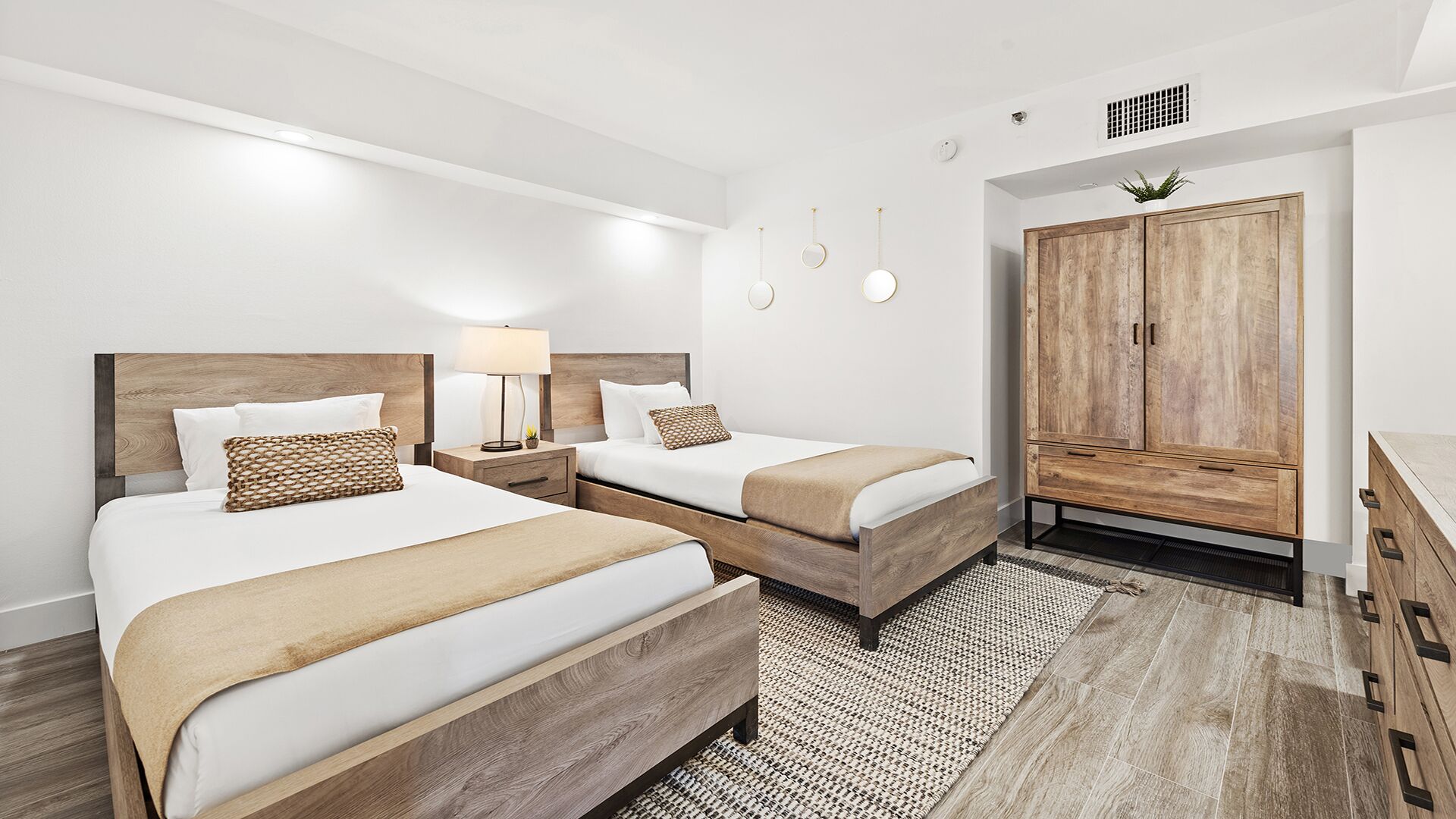 A hotel room with two beds, a wardrobe, and a small desk.