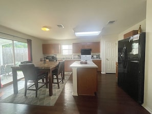 A kitchen with a dining area, wooden cabinets, a black refrigerator, and a window providing natural light.