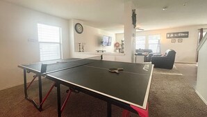 A ping pong table in a living room with a couch and a TV in the background. - Spacious 5BR • 11 Beds • Sleeps 15 • Fenced Yard w/Grill – Great July Rates! (Pflugerville)