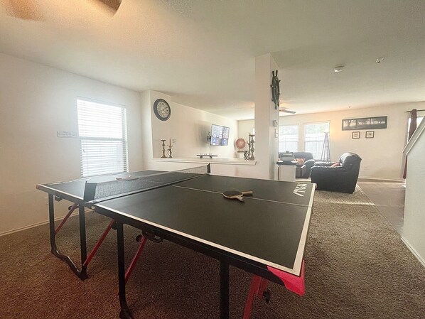 A ping pong table in a living room with a couch and a TV in the background.