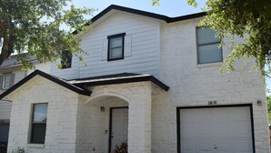 A two-story house with a white exterior, a garage, and a front entrance with a small porch. - Spacious 5BR • 11 Beds • Sleeps 15 • Fenced Yard w/Grill – Great July Rates! (Pflugerville)