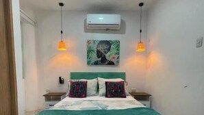 A bedroom with a bed, two bedside tables, an air conditioner, and two pendant lights. - Casa Colors (Cartagena)