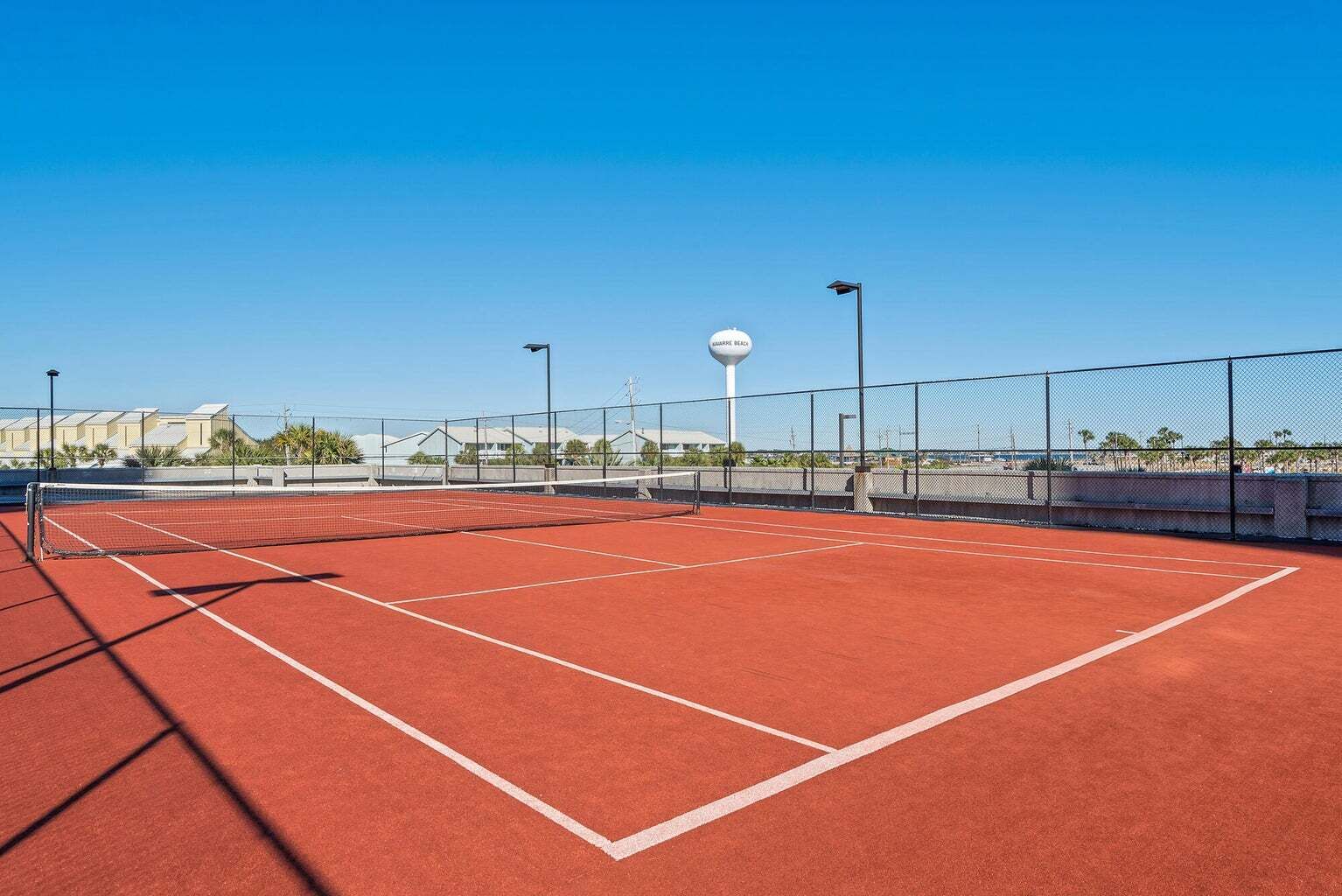 A tennis court with a net, surrounded by a fence and street lamps.