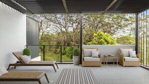 Zona d'estar exterior moderna amb mobiliari de vimet, una finestra gran i vista a arbres.