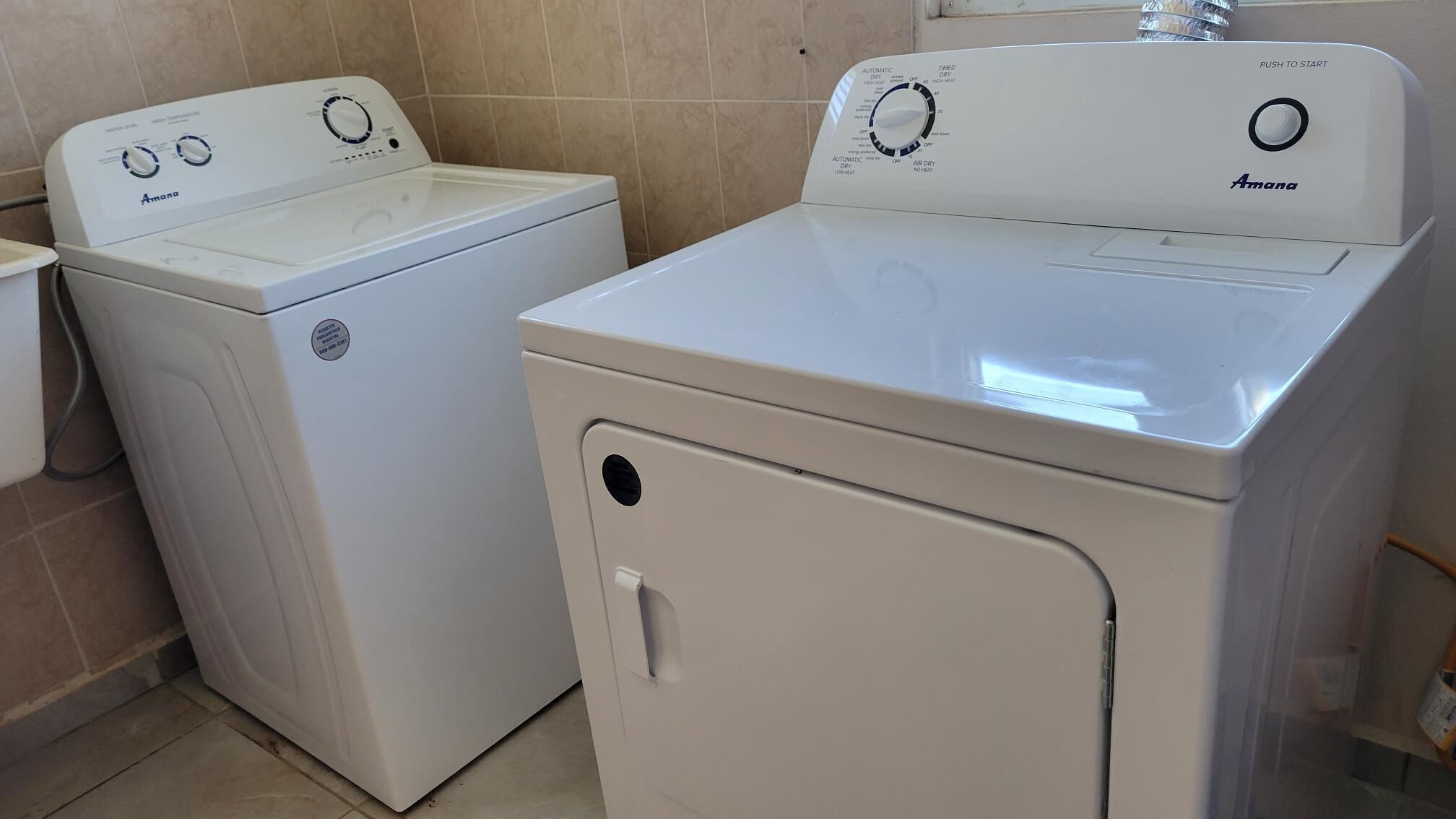Two white front-loading washing machines in a bathroom with beige tiles.