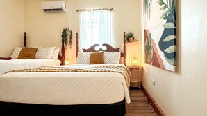 A hotel room with two beds, a brick-patterned floor, a window with sheer curtains, and a wall-mounted air conditioner. - Two floor combo unit (San Juan)