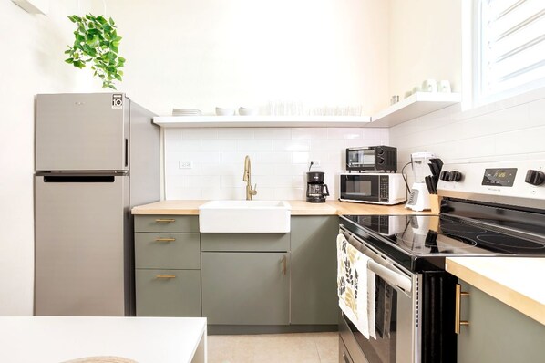 A compact kitchen with a refrigerator, sink, microwave, coffee maker, and oven.