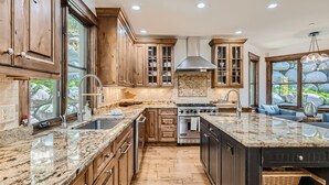 A kitchen with wooden cabinets, granite countertops, a stove, and a large window overlooking a rocky landscape. - Gorgeous Mountain Residence, Spectacular Views, Fire Pit (Vail)