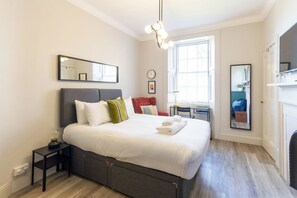 A modern bedroom with a large bed, bedside tables, a desk, and a mirror.