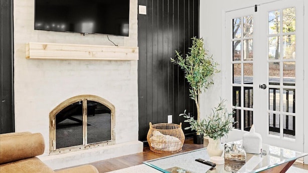 Een woonkamer met een open haard, een televisie erboven en een deur naar buiten.
