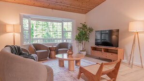 Una sala de estar moderna con un amplio ventanal, un televisor de pantalla plana y muebles de madera.