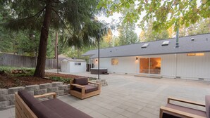Un patio al aire libre con mobiliario de madera, una pared de piedra y un edificio de fachada blanca al fondo.