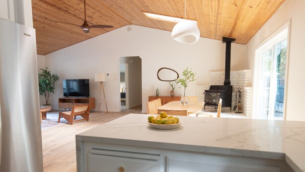 Una cocina amplia con techo de madera, una isla grande con un frutero, horno empotrado y televisión al fondo.