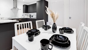 Una cocina moderna con armarios negros, una encimera blanca y una zona de comedor con una mesa dispuesta para cuatro comensales.