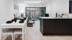 Una cocina moderna con una isla central, una mesa de comedor blanca con sillas y un sofá gris.