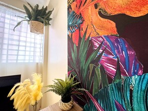 Una habitación con ventana, una pared con un mural tropical y una mesa de madera con una planta en maceta.
